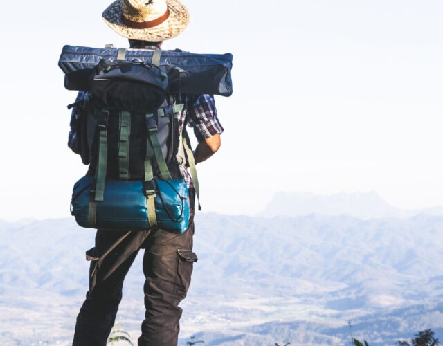 Tourist from mountain top. sun rays. man wear big backpack agai